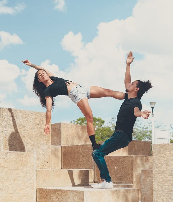 A woman performing a balanced yoga pose in a dark cyan room.